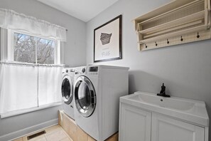 A laundry room with a front-loading washer and dryer, a sink, and a window with a white curtain. - Cedar Peak - Pool, Hot Tub & Gym, Sleeps 24 (Cheatham County)