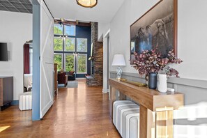 Un hall d’entrée spacieux, doté d’un plancher en bois, d’un mur décoratif en pierre et d’une grande fenêtre qui laisse entrer la lumière naturelle.