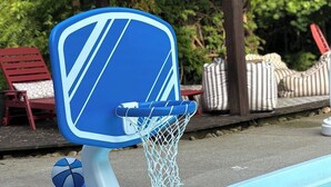 Un aro de baloncesto junto a una piscina, con un tablero azul y una red.