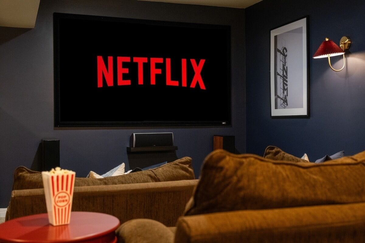 A dark room with a large screen displaying 'NETFLIX' in red letters, a framed picture on the wall, and a popcorn container on a small table.