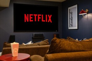 A dark room with a large screen displaying 'NETFLIX' in red letters, a framed picture on the wall, and a popcorn container on a small table. - Cedar Peak - Hot Tub, Sauna, Theater, Sleeps 24 (Cheatham County)