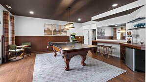 Una mesa de billar en una habitación que incluye una cocina, un bar y una zona de estar con vistas al exterior.