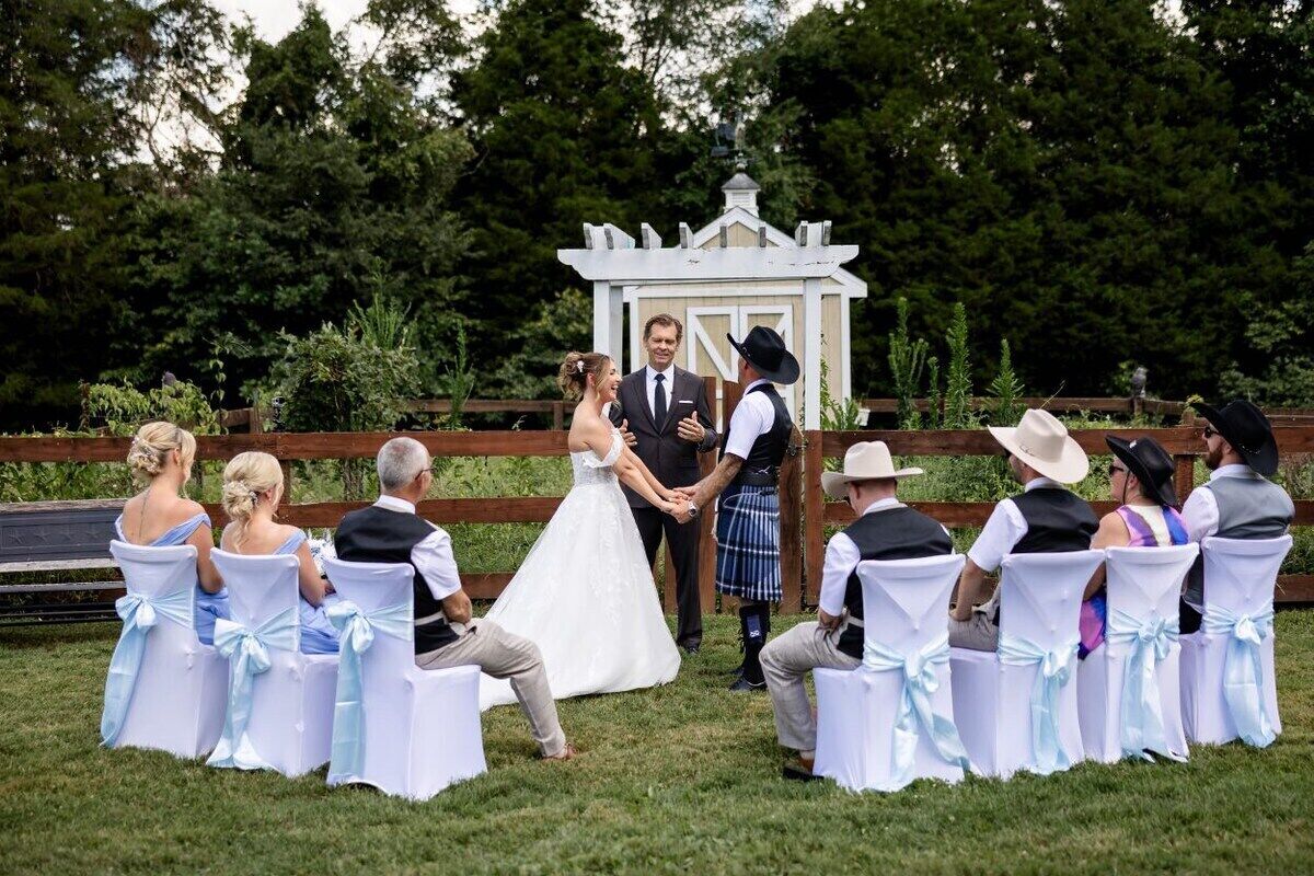 Une cérémonie de mariage en plein air, les invités étant assis sur des chaises recouvertes de housses blanches.