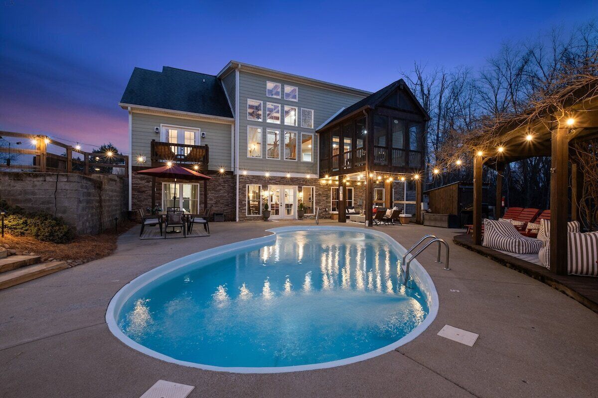 Una casa de dos pisos con piscina, mobiliario exterior e iluminación con guirnaldas.