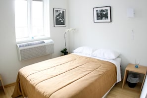 A bedroom with a bed, a window with an air conditioner, and two framed pictures on the wall. - Queen West Jazz Stay (Toronto)
