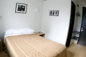A bedroom with a bed, a nightstand, a framed photo, a door, and a small shelf. - Queen West Jazz Stay (Toronto)