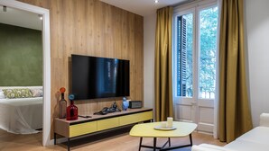 A modern hotel room with a wooden panel wall, a flat-screen TV, a yellow console table, a bed with patterned pillows, and a window with curtains. - Design Sun and Rooftop Wi-Fi Fast Sagrada Familia (Barcelona)
