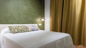 A neatly made bed with white bedding and patterned pillows, a green textured wall, a gold curtain, and a wall-mounted light fixture. - Design Sun and Rooftop Wi-Fi Fast Sagrada Familia (Barcelona)