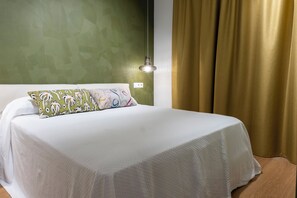 Ein ordentlich bezogenes Bett mit weißer Bettwäsche und gemusterten Kissen, eine Wand mit einer grünen Struktur, ein goldener Vorhang und eine Wandleuchte.
