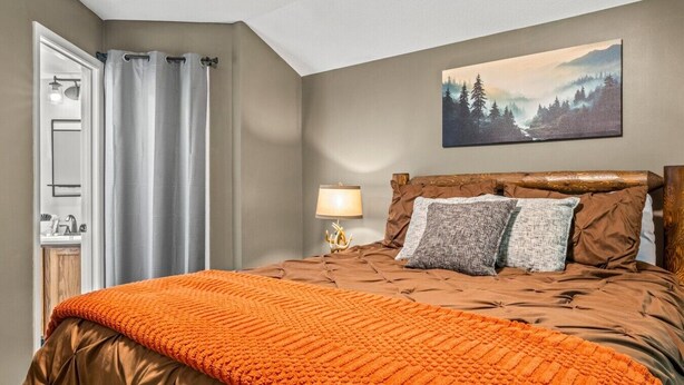 A bedroom with a bed, a painting, a nightstand, and a lamp. - Ember Hollow | Hot Tub • Near Gatlinburg • Pets (Gatlinburg)