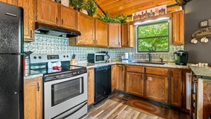 A kitchen with wooden cabinets, a black refrigerator, a stove, a microwave, and a coffee maker. - Ember Hollow | Hot Tub • Near Gatlinburg • Pets (Gatlinburg)