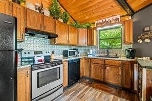 A kitchen with wooden cabinets, a black refrigerator, a stove, a microwave, and a coffee maker. - Ember Hollow | Hot Tub • Near Gatlinburg • Pets (Gatlinburg)