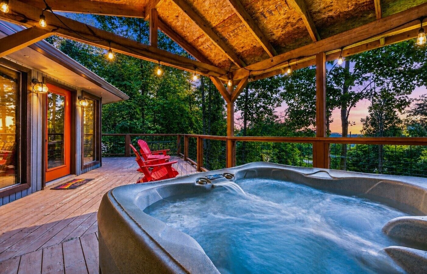 A hot tub with a wooden deck and red chairs, surrounded by a wooden pergola with string lights.