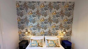 Ein Schlafzimmer mit gemustertem Wandpapier, einem Bett mit zwei Kissen, Nachttischen und Lampen.