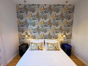 A bedroom with a patterned wallpaper, a bed with two pillows, bedside tables, and lamps. - Nomad friendly • Wi-Fi Fast • Rooftop • Center BCN (Barcelona)