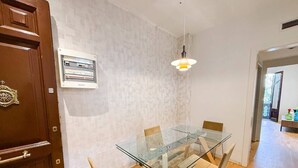 Ein Essbereich mit einem Glastisch und Stühlen, einer Holztür, einer Wandleuchte und einem gerahmten Zertifikat an der Wand.
