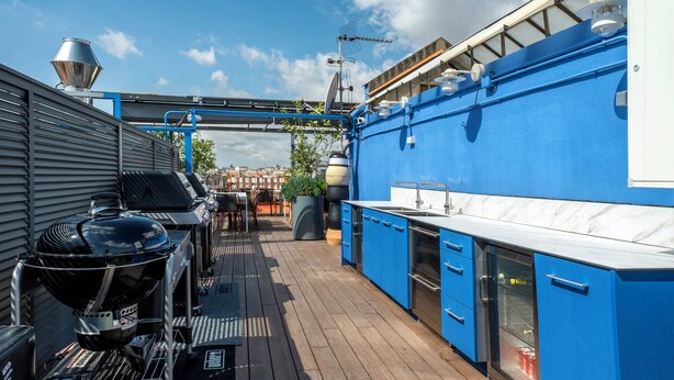 Eine Dachterrasse mit Grillplatz, Sitzgelegenheiten im Freien und einer blauen Küchenzeile.
