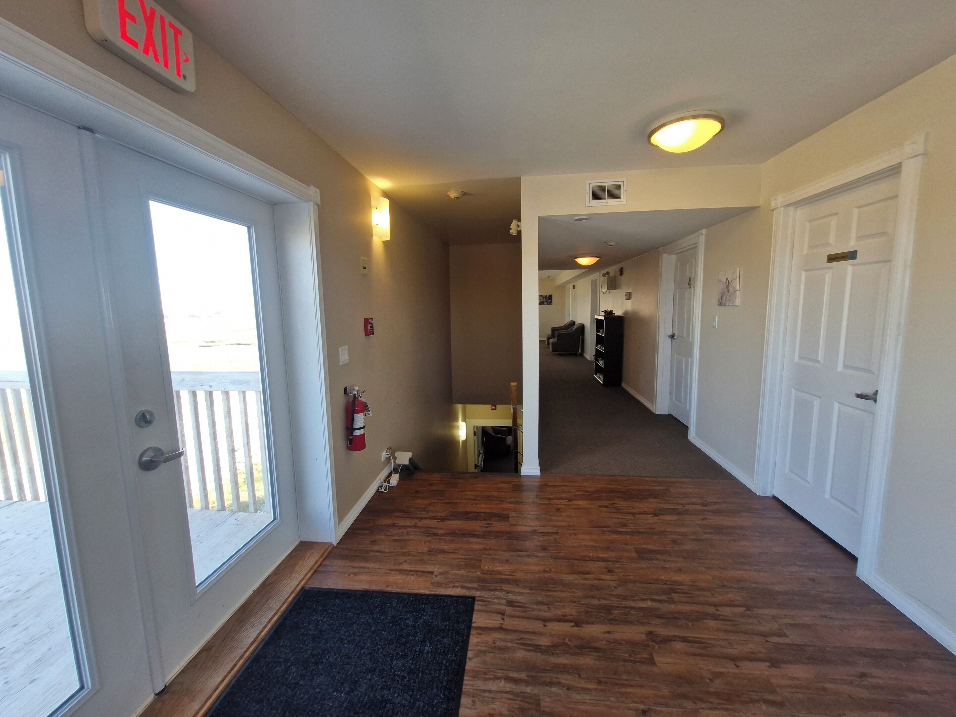 A hallway with a wooden floor, white doors, and an exit sign.