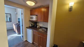 A compact kitchen with wooden cabinets, a microwave, a coffee maker, and a sink.