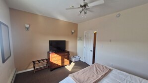 A bedroom with a bed, a dresser, a television, a ceiling fan, and a door. - Umingmak Lodge Bed And Breakfast (Cambridge Bay)