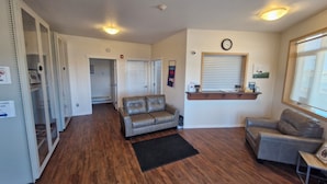 A spacious living area with a leather sofa, a small table, and a window with blinds. - Umingmak Lodge Bed And Breakfast (Cambridge Bay)