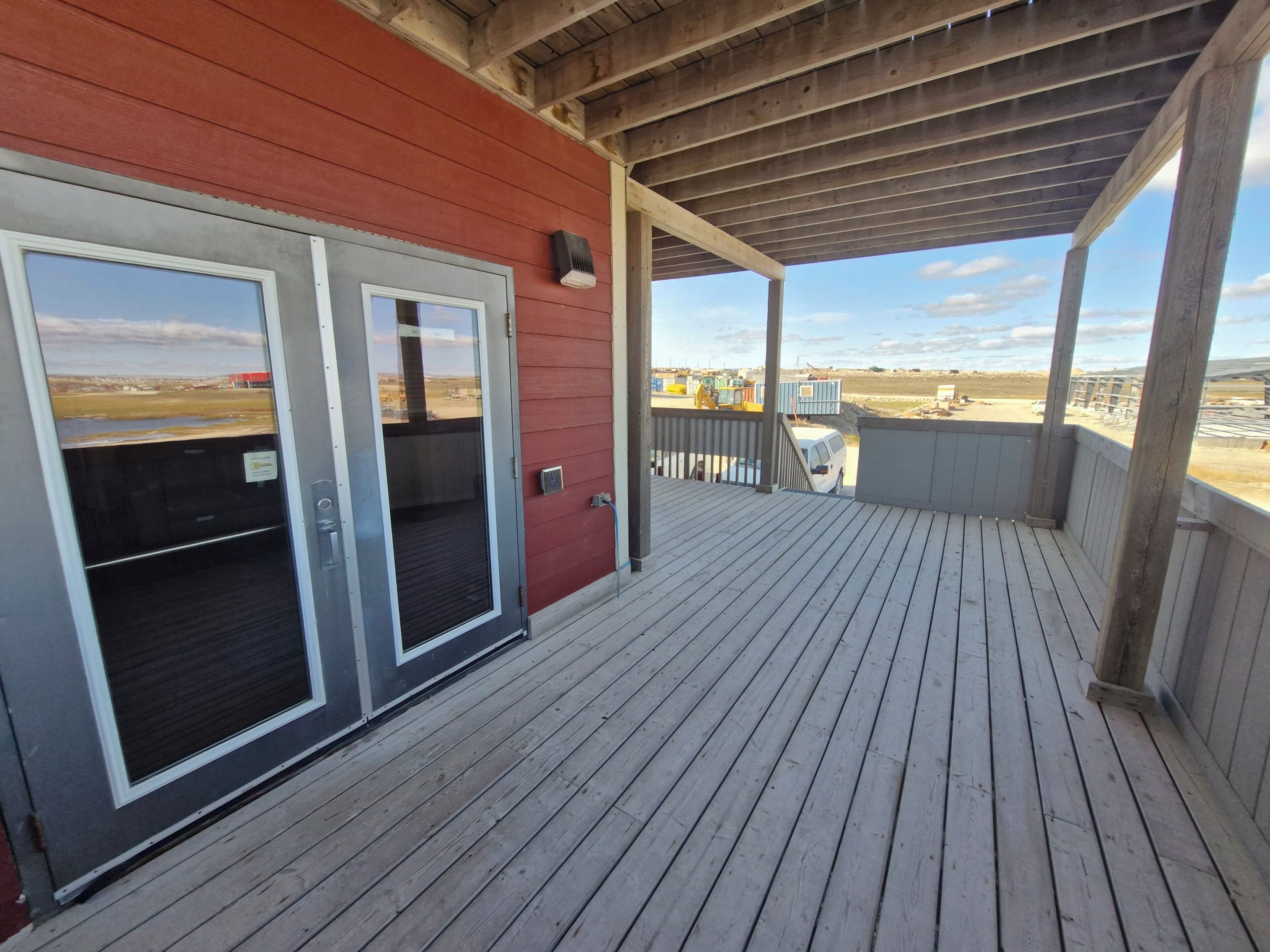 Una terraza de madera con un espacio cubierto, un edificio rojo y vistas a una obra en construcción.