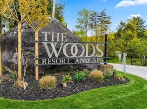 Un grand rocher sur lequel est apposée une plaque indiquant « The Woods Resort and Spa », entouré d’un jardin aménagé avec différentes espèces de plantes.