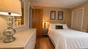 A bedroom with a bed, a nightstand with a lamp, a dresser, and a door leading to another room. - 7 minutes from the Killington Base Lodge and seconds away from the best restaurants and nightlife! (Killington)