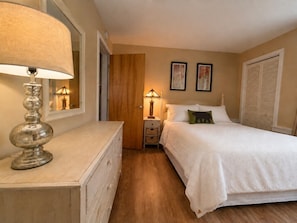 A bedroom with a bed, a nightstand with a lamp, a dresser, and a door leading to another room. - 7 minutes from the Killington Base Lodge and seconds away from the best restaurants and nightlife! (Killington)
