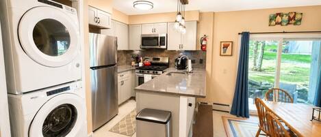 A compact kitchen with a built-in washer and dryer, stainless steel appliances, and a dining area with a view of the outdoors.