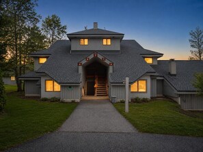 Ein modernes, zweistöckiges Haus mit einem zentralen Eingangsbereich, einer sichtbaren Treppe und einem gepflegten Rasen.