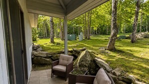 An outdoor patio area with two wicker chairs and a glass-top table, surrounded by a stone wall and a grassy lawn with trees. - 7 minutes from the Killington Base Lodge and seconds away from the best restaurants and nightlife! (Killington)