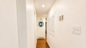 En smal hall med vita väggar och trägolv, som leder till en dörr med ett fönster.