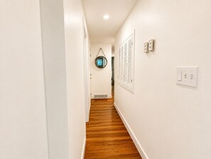 A narrow hallway with white walls and wooden flooring, leading to a door with a window. - Near Killington & Woodstock | Game Room, Fireplace (Bridgewater)