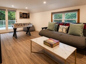 A living room with a foosball table, a sofa with cushions, and a coffee table with a board game. - Near Killington & Woodstock | Game Room, Fireplace (Bridgewater)