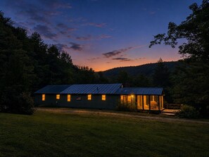 A single-story building with a metal roof, a porch with seating, and a flag on the front. - Near Killington & Woodstock | Game Room, Fireplace (Bridgewater)