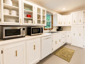 A kitchen with white cabinets, two built-in microwaves, a coffee maker, and a window with a view of greenery. - Near Killington & Woodstock | Game Room, Fireplace (Bridgewater)