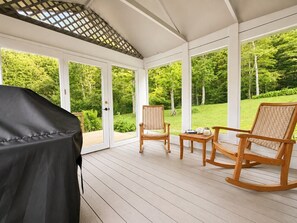 A covered patio with a grill, two rocking chairs, and a small table with decorative items. - Near Killington & Woodstock | Game Room, Fireplace (Bridgewater)