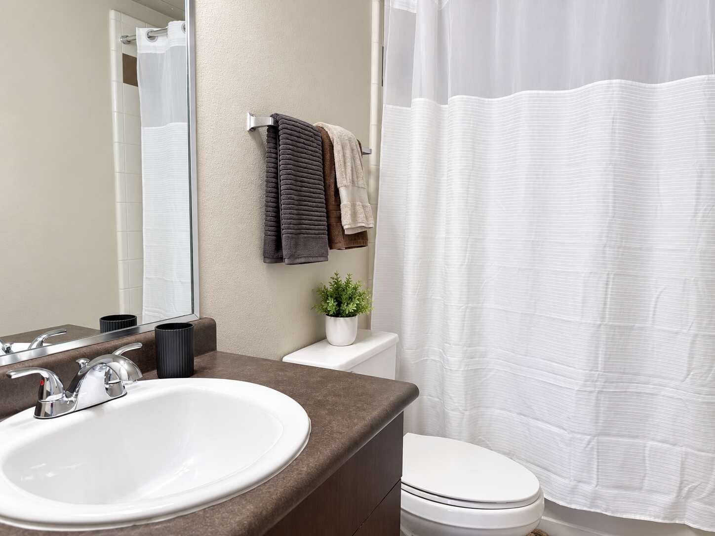 A bathroom with a white sink, a toilet, a shower curtain, and a mirror.