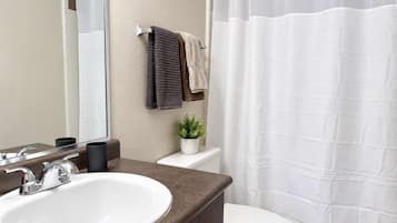 A bathroom with a white sink, a toilet, a shower curtain, and a mirror.