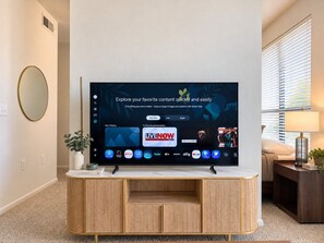 A flat-screen TV mounted on a wooden cabinet with a TV Plus Recommendation screen displaying various streaming services.