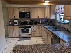 A kitchen with wooden cabinets, a stove, microwave, and granite countertops. - A Relaxing Denton Oasis (Denton)