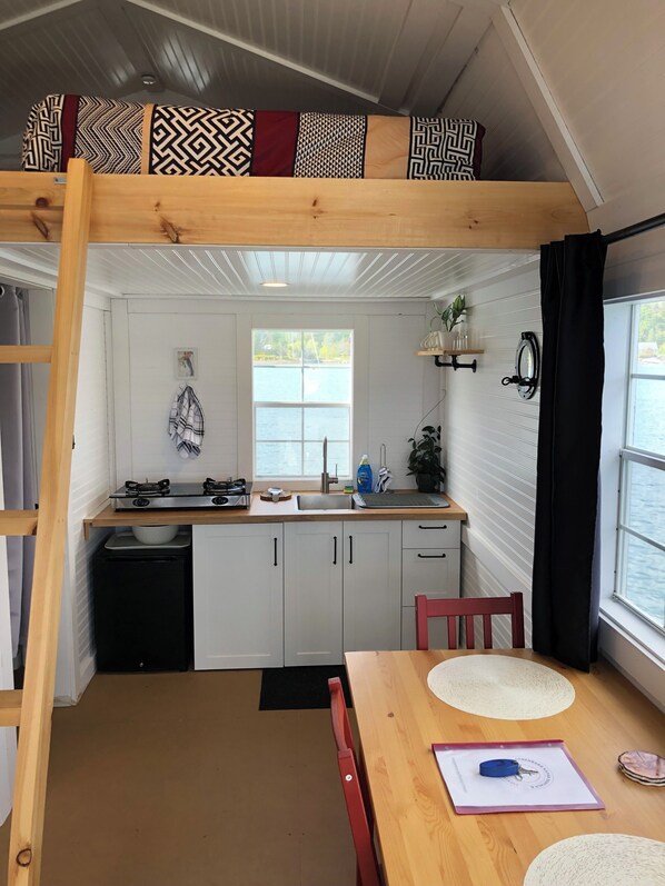 A compact kitchen with a wooden table, a red chair, and a bunk bed above.