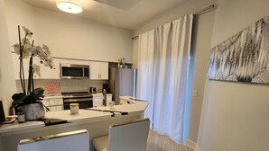 A modern kitchen with white cabinets, a microwave, and a refrigerator. There is a dining area with a white table and chairs. - Sunshine, Comfort & Magic in Orlando (Orlando)