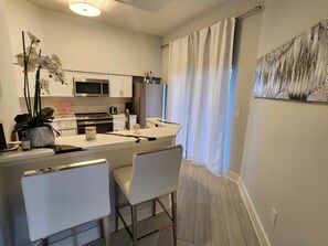 Eine moderne Küche mit weißen Schränken, einer Mikrowelle und einem Kühlschrank. Es gibt einen Essbereich mit einem weißen Tisch und Stühlen.