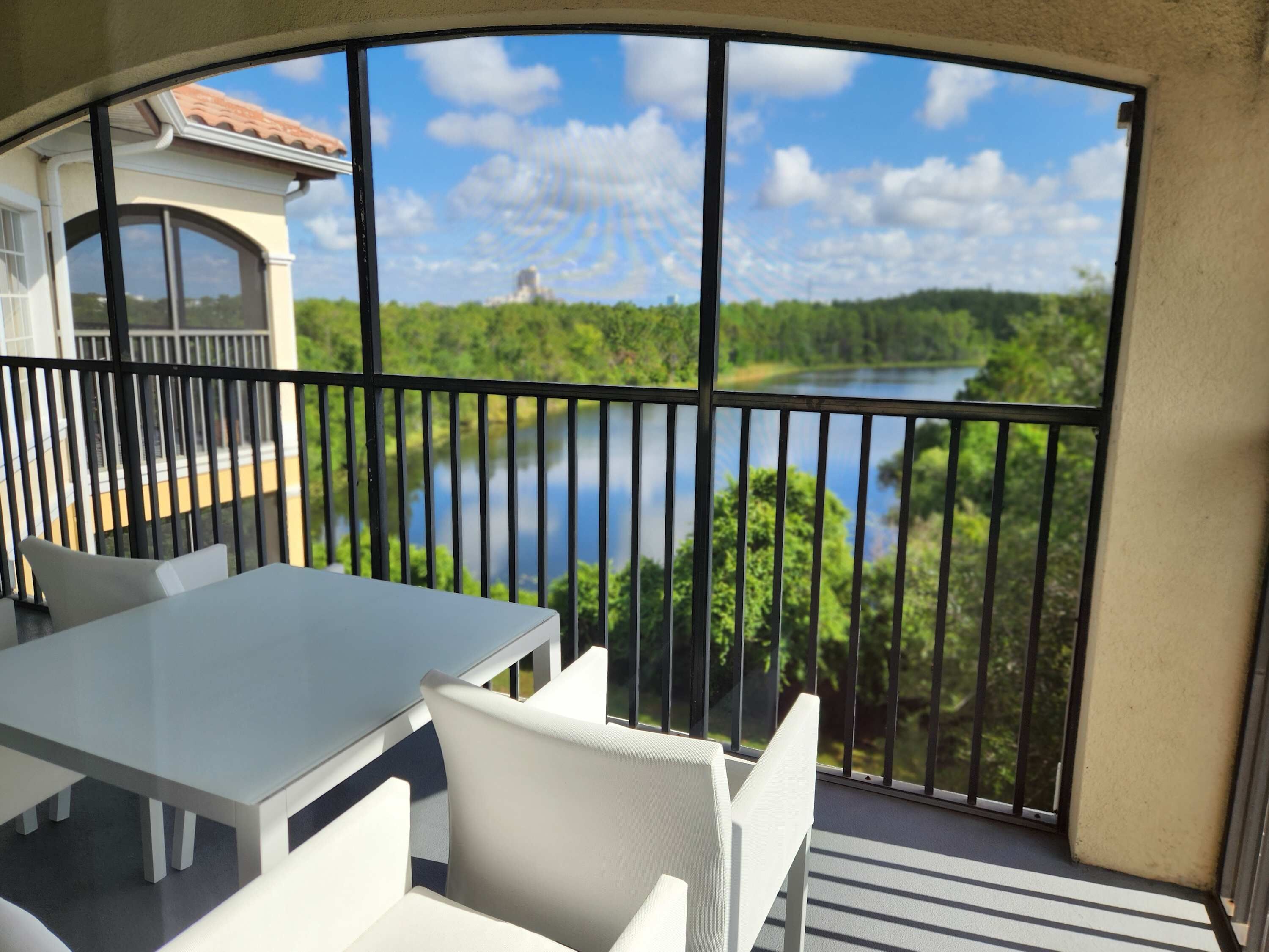 A balcony with a table and chairs, overlooking a lake and greenery.