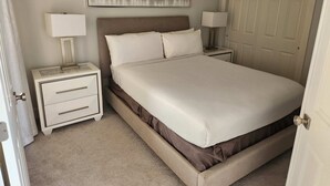 A bedroom with a bed, two bedside tables with lamps, a door, and a wall-mounted artwork. - Sunshine, Comfort & Magic in Orlando (Orlando)