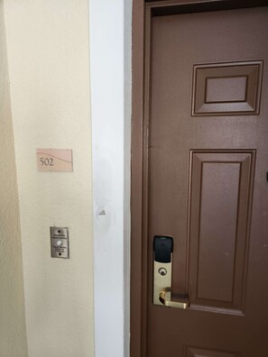 Eine braune Tür mit einem Zahlenschloss, einem Schild mit der Zimmernummer und einem Knopf für barrierefreies Zimmer.