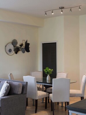 A dining area with a round table, white upholstered chairs, a grey sofa, and a wall-mounted light fixture. - A Relaxing Getaway & More! M452 (Orlando)