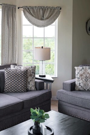 A living room with two grey sofas, patterned cushions, a table lamp, and a window with curtains. - A Relaxing Getaway & More! M452 (Orlando)